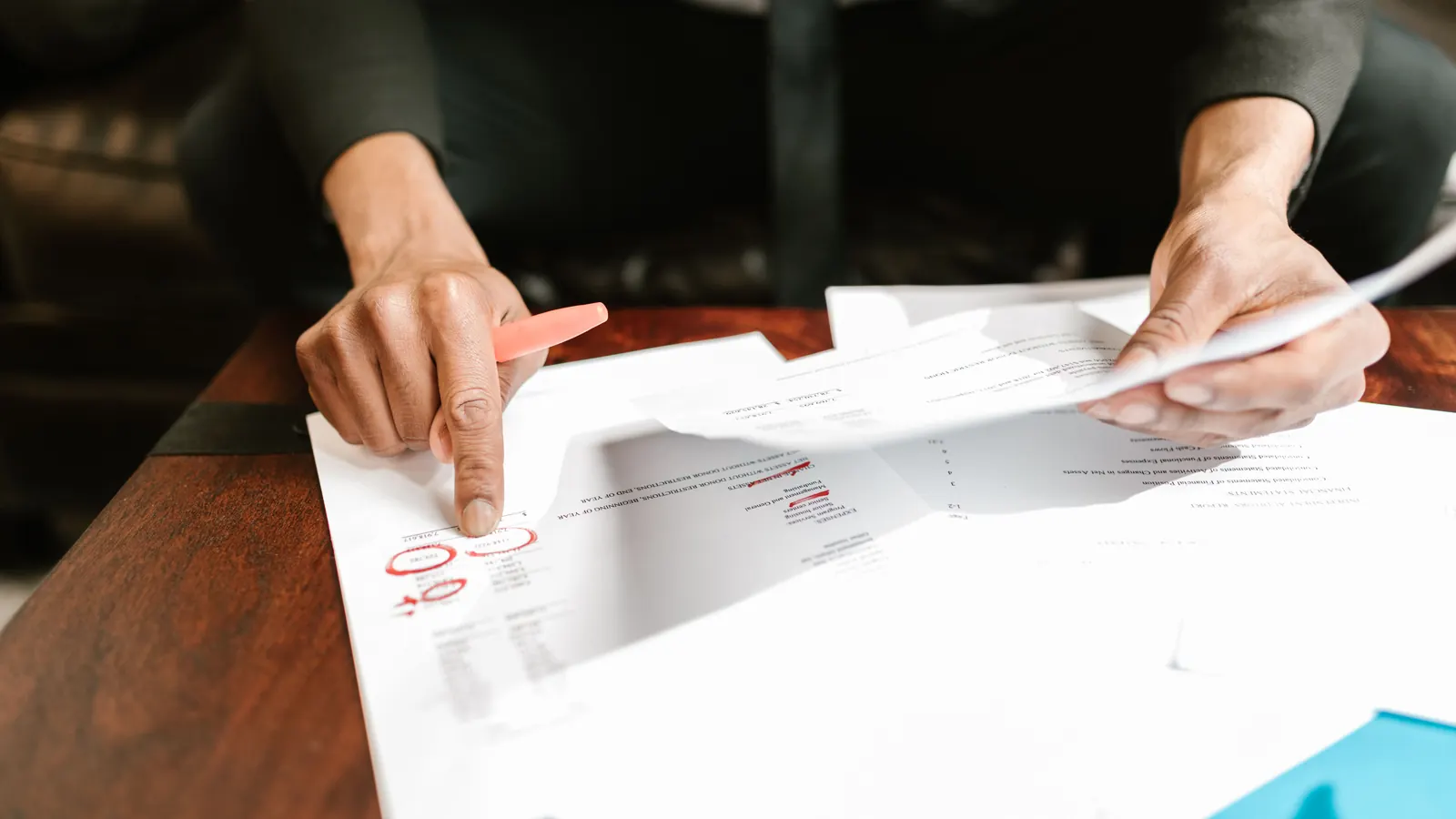 A hand holding a pen pointing at figures on a printed document on a dark desk