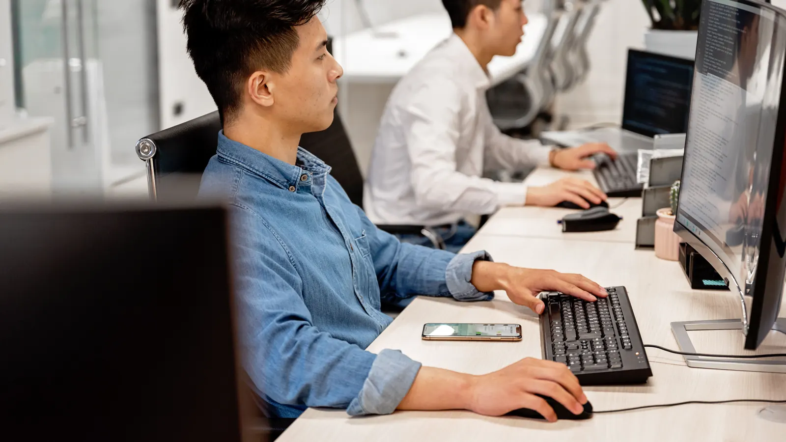 Two office workers at desks reviewing figures on their computer screens