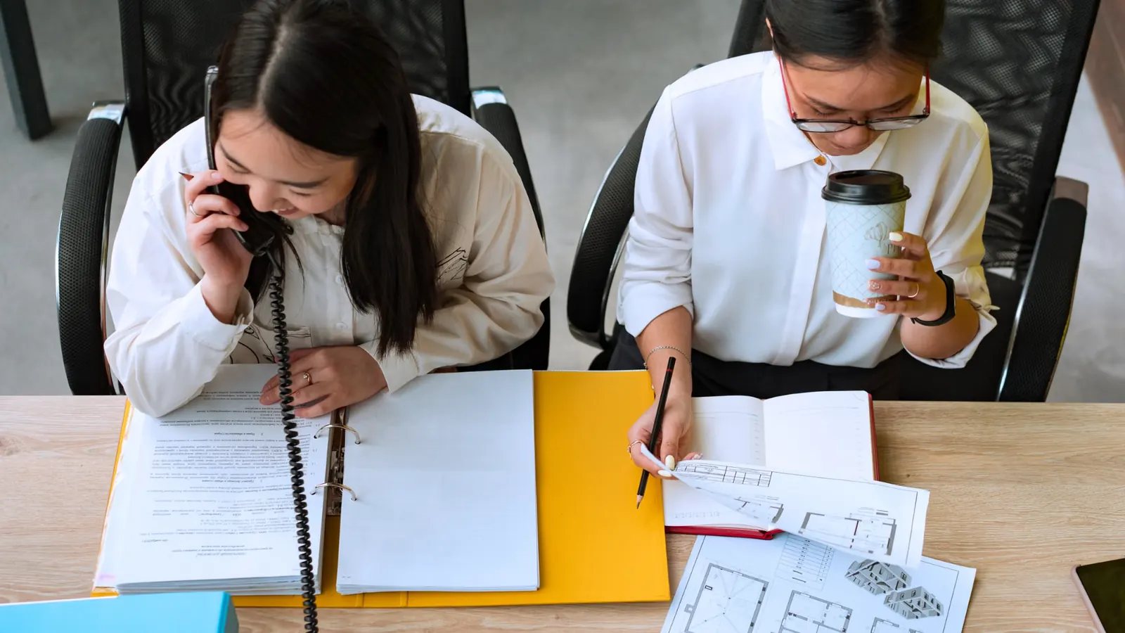 Two colleagues reviewing paperwork and architectural plans at a desk