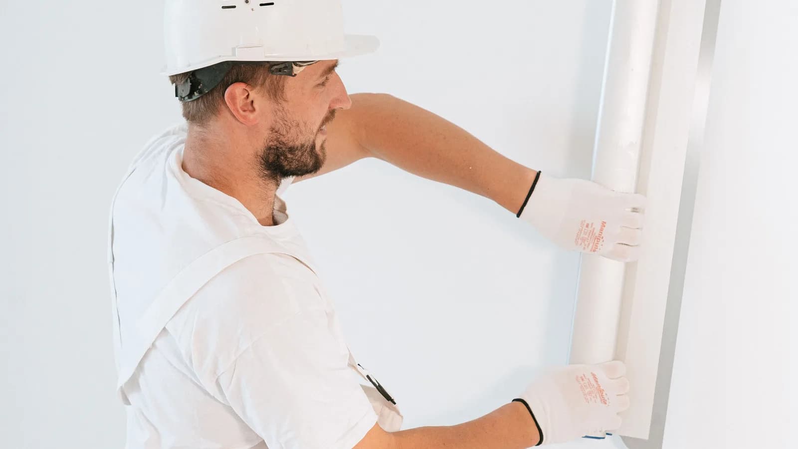 Tradesperson in a hard hat and gloves fitting a panel during a fit-out