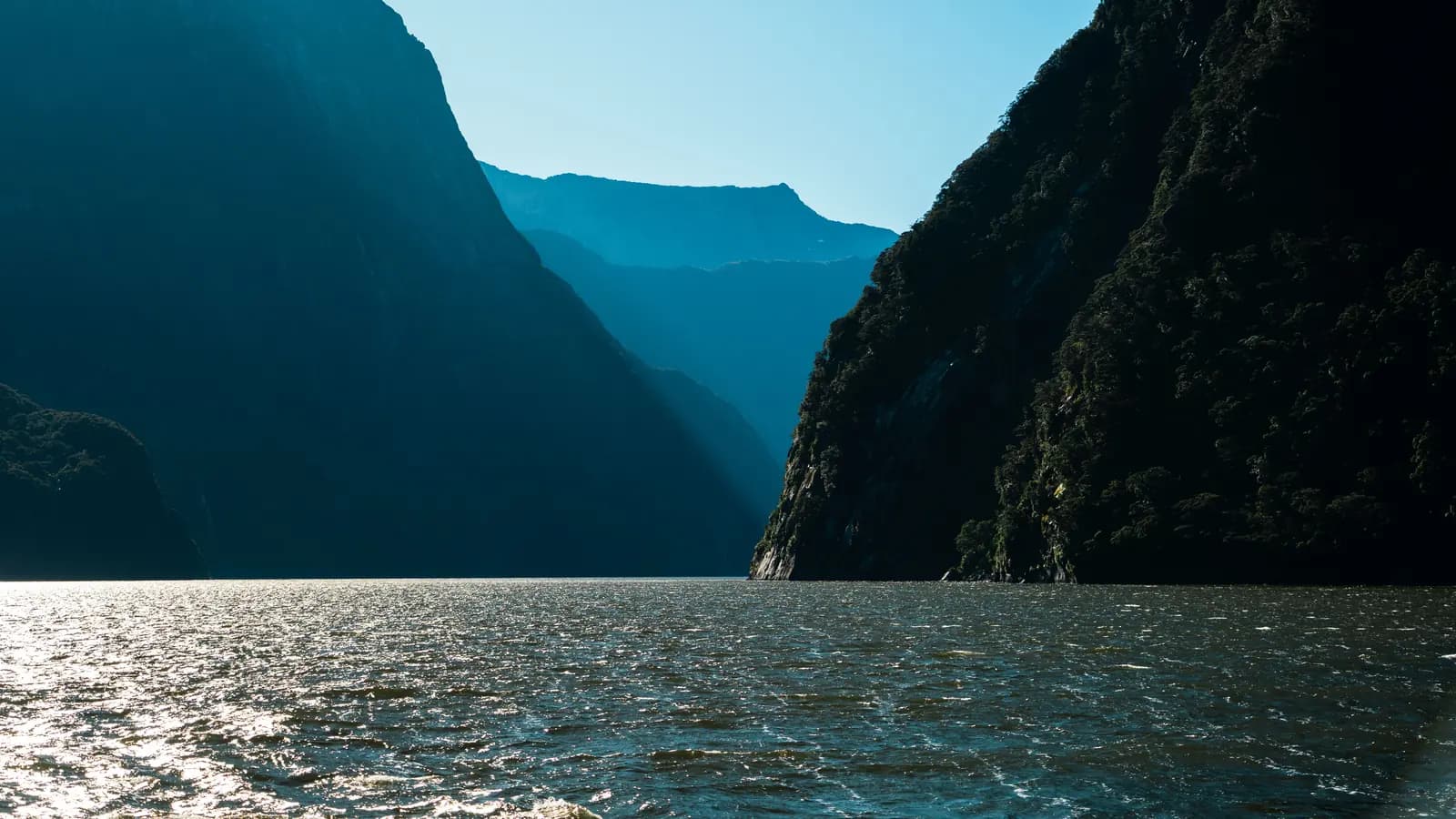 Sunlight on the water at a New Zealand fiord, framed by steep cliffs