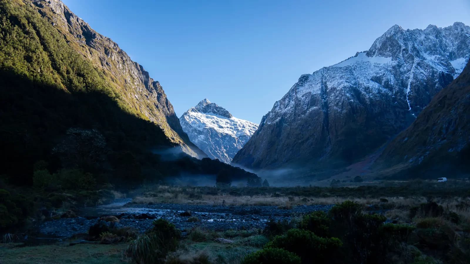 Misty New Zealand mountain valley with a snow-capped peak in the distance