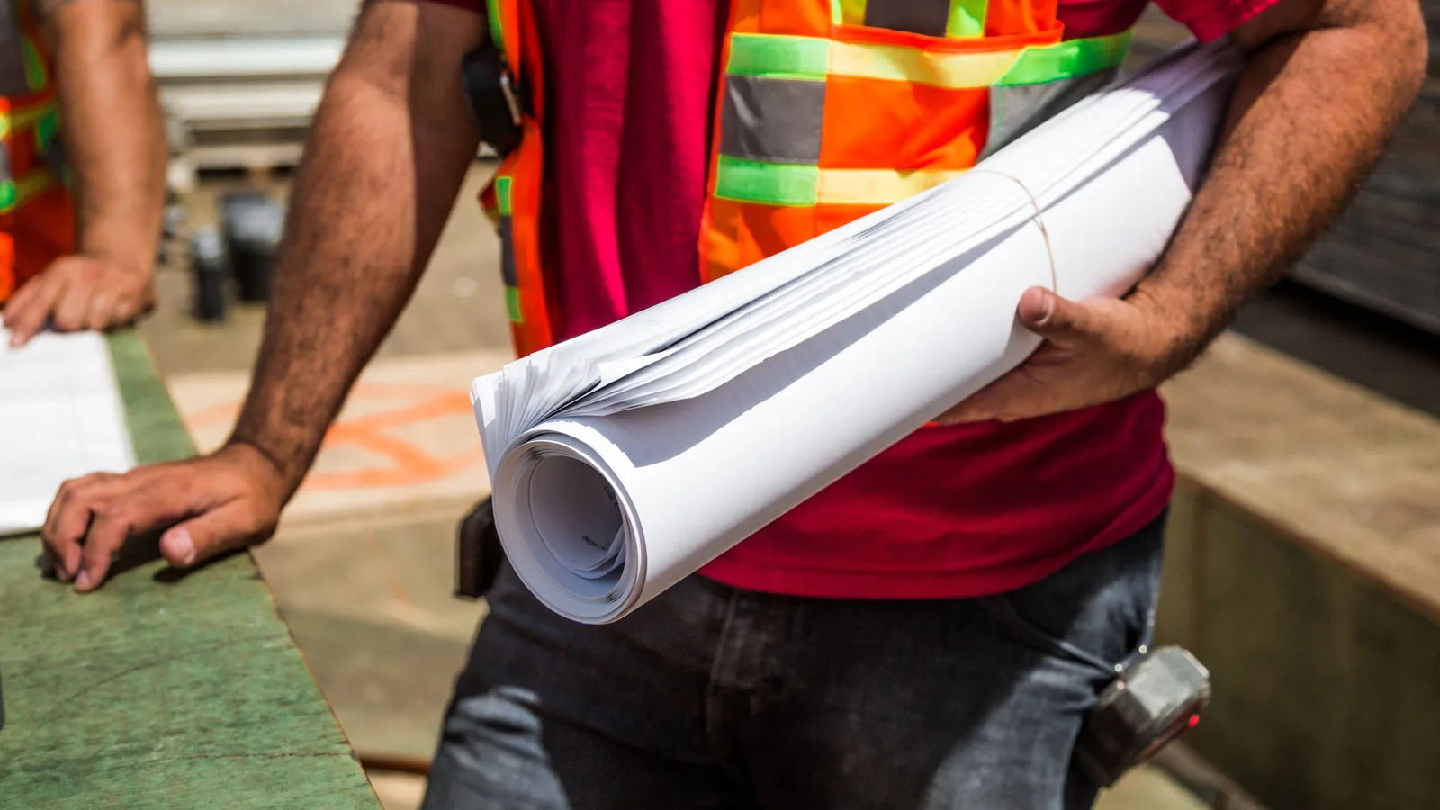 Construction worker in a hi-vis vest carrying a rolled set of building plans