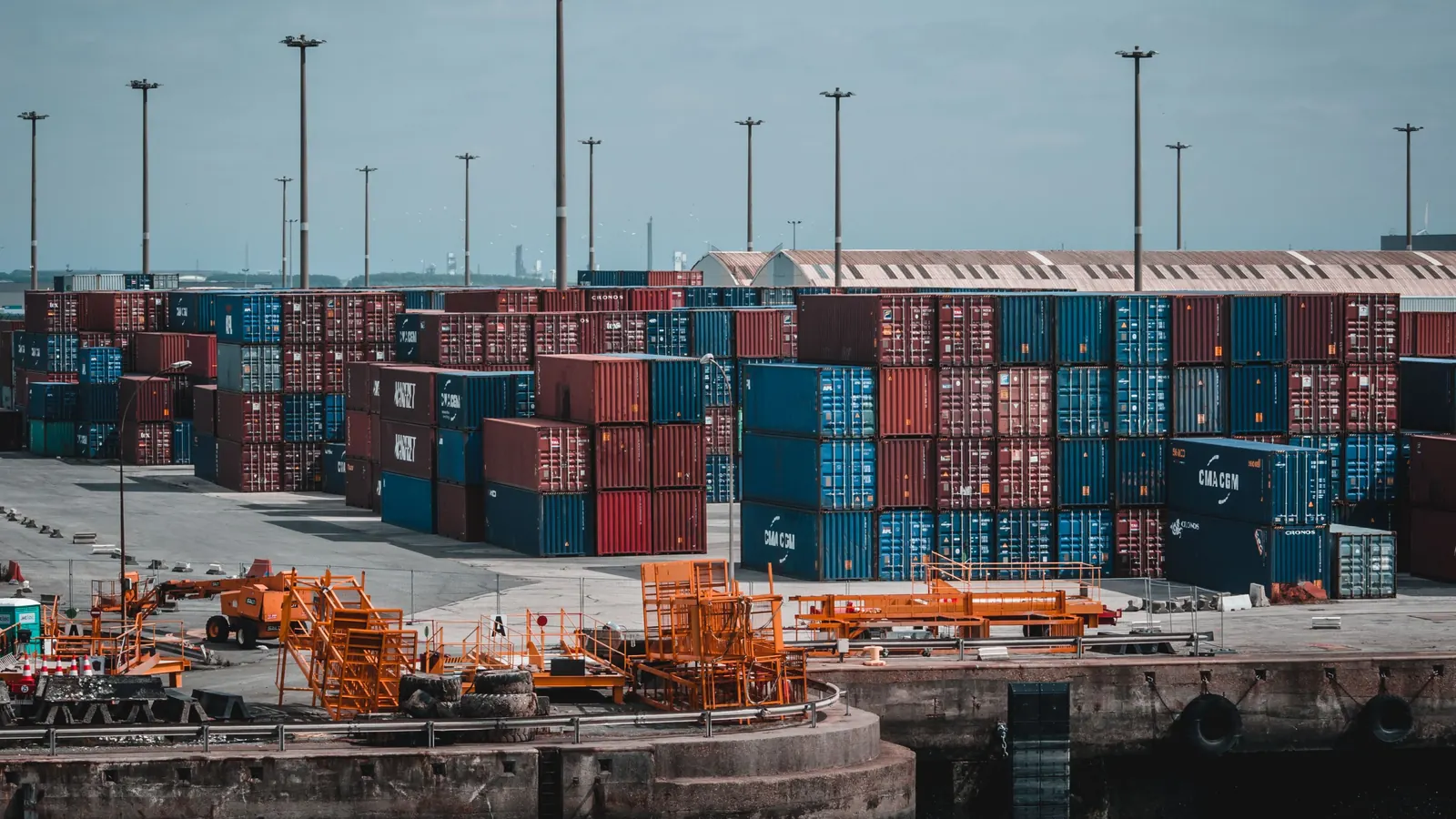 Rows of stacked shipping containers at a port beside cranes and cargo equipment