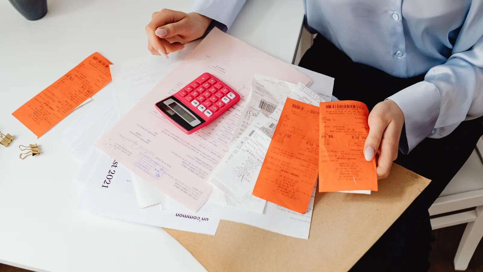 A person sorting payment slips and receipts beside a pink calculator