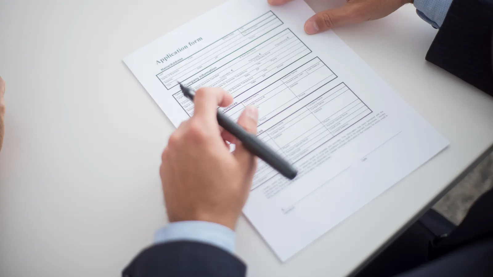 Close-up of hands filling out a business credit application form with a pen