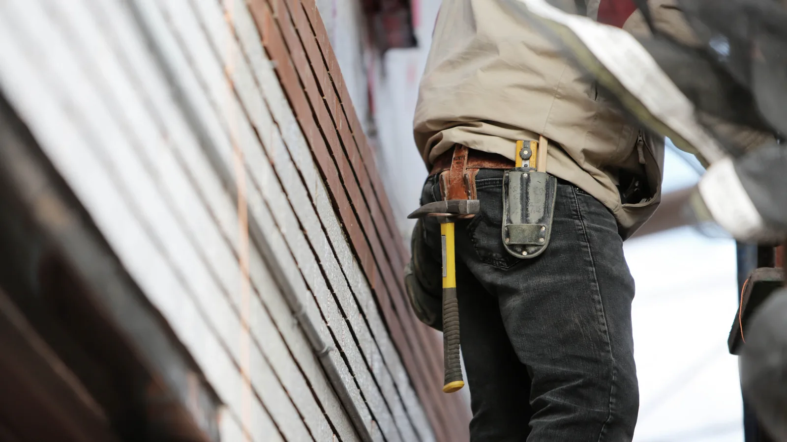 Close-up of a tradesperson's tool belt and hammer against a brick wall on a building site