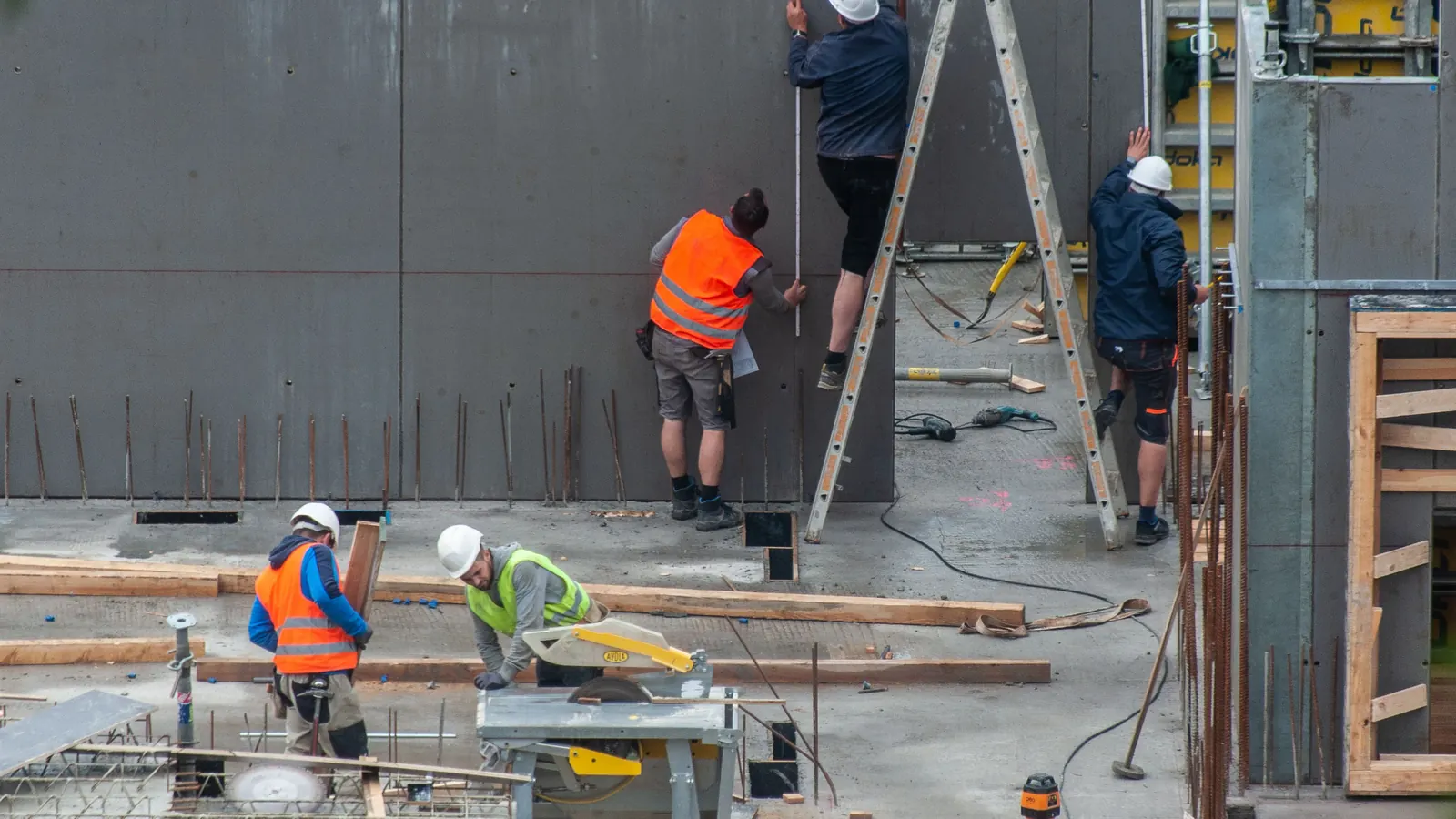 Construction workers in hi-vis and hard hats measuring formwork on a building site