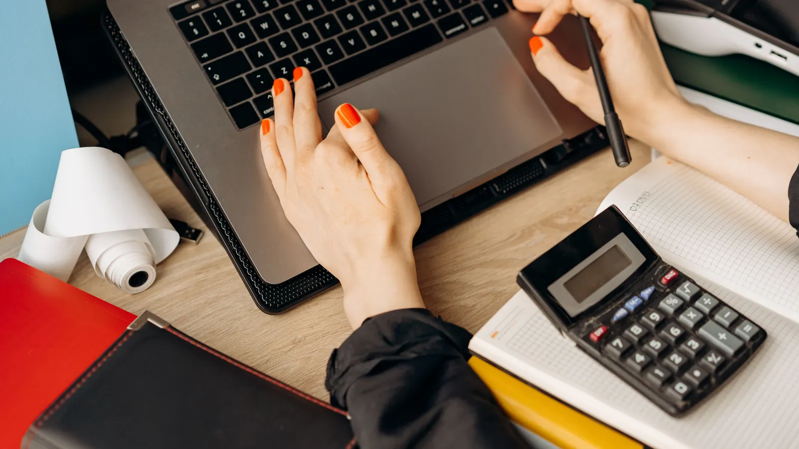 A person working at a laptop with a calculator and notebook on the desk
