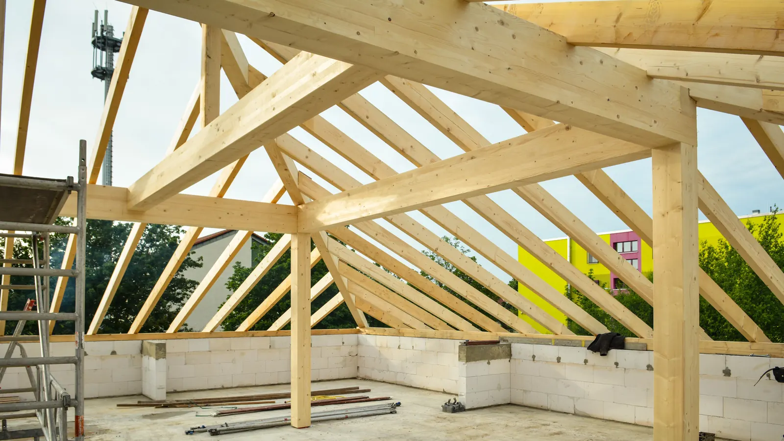 Timber roof trusses framed over a concrete floor on a building site, with scaffolding at the edge