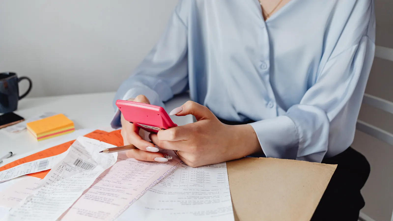 Close-up of hands using a calculator alongside printed receipts on a desk