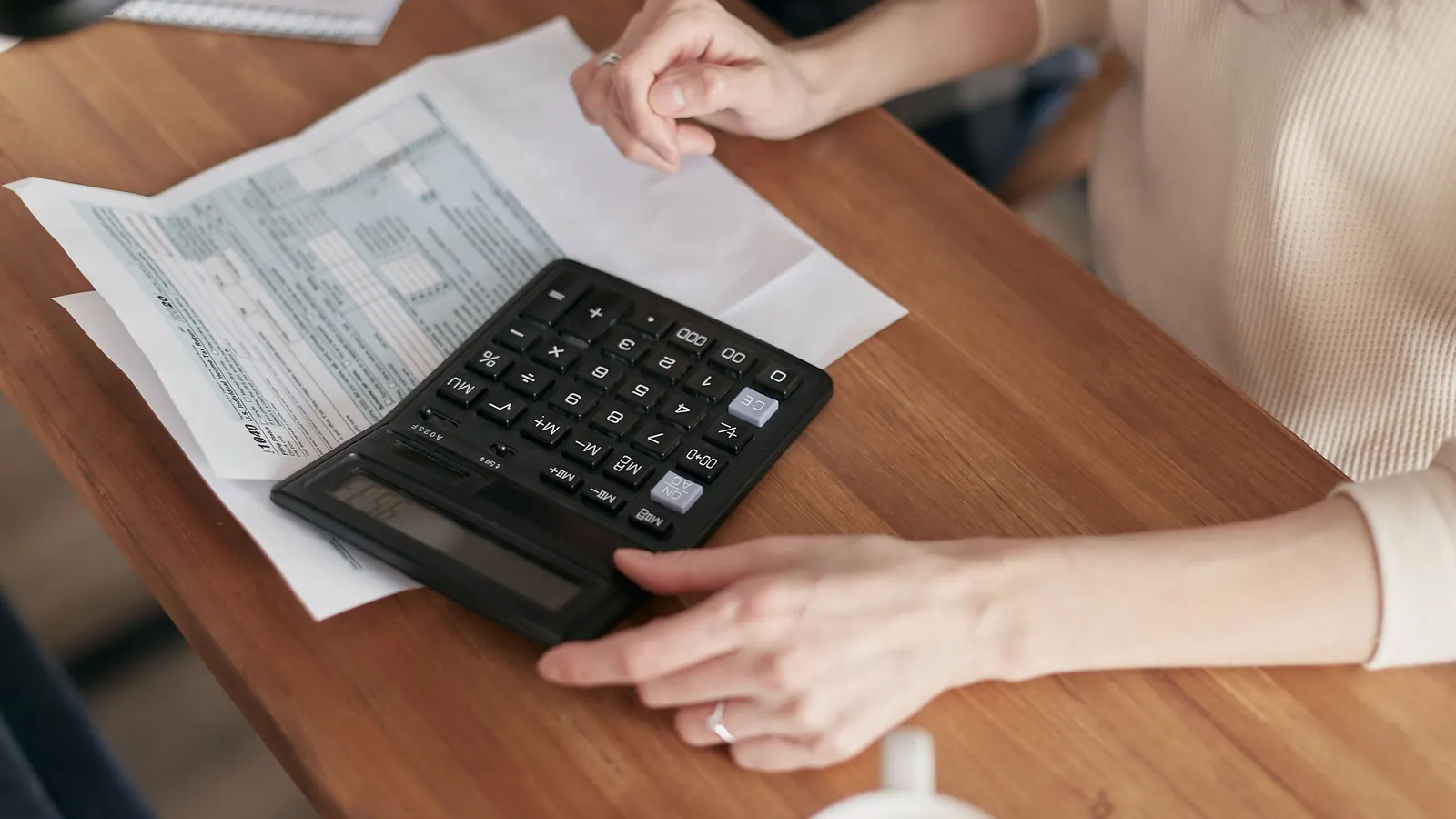 A person working through bills with a calculator at a wooden table