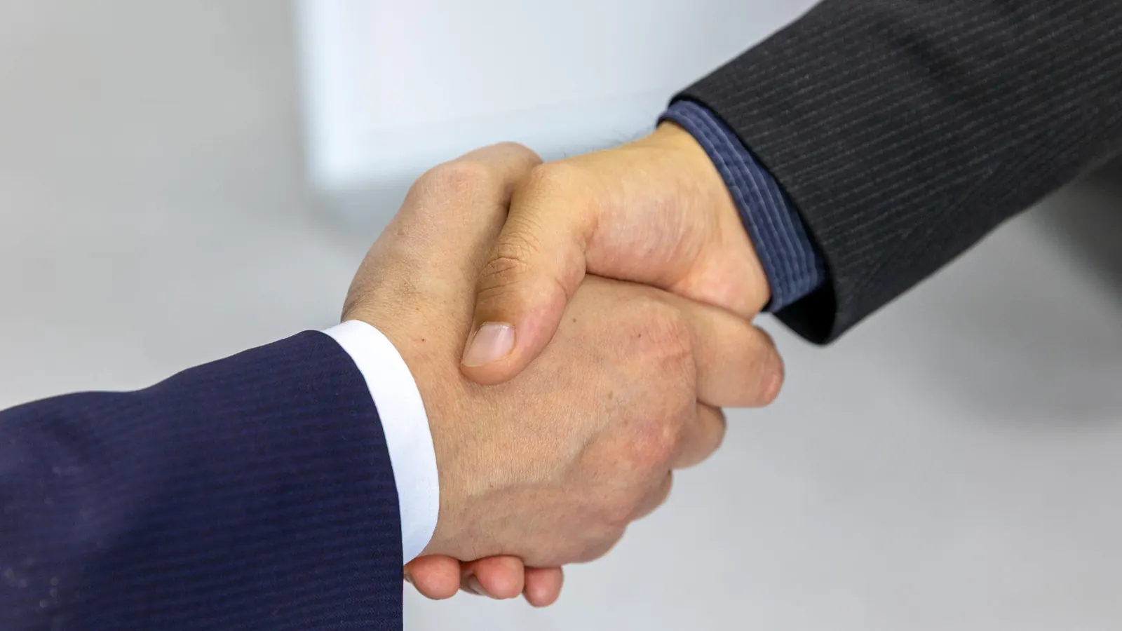 Close-up of two people in suits shaking hands against a pale background