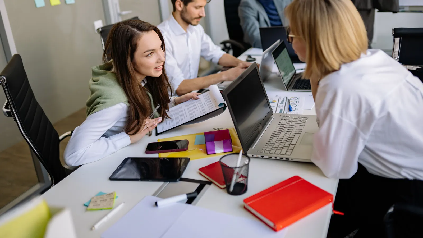 Colleagues discussing paperwork and laptops together at a shared office desk