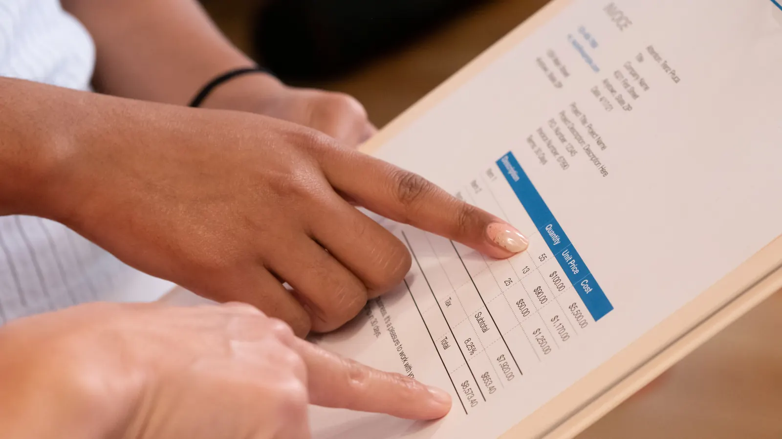 Two people pointing at the line items, subtotal and total on a printed invoice