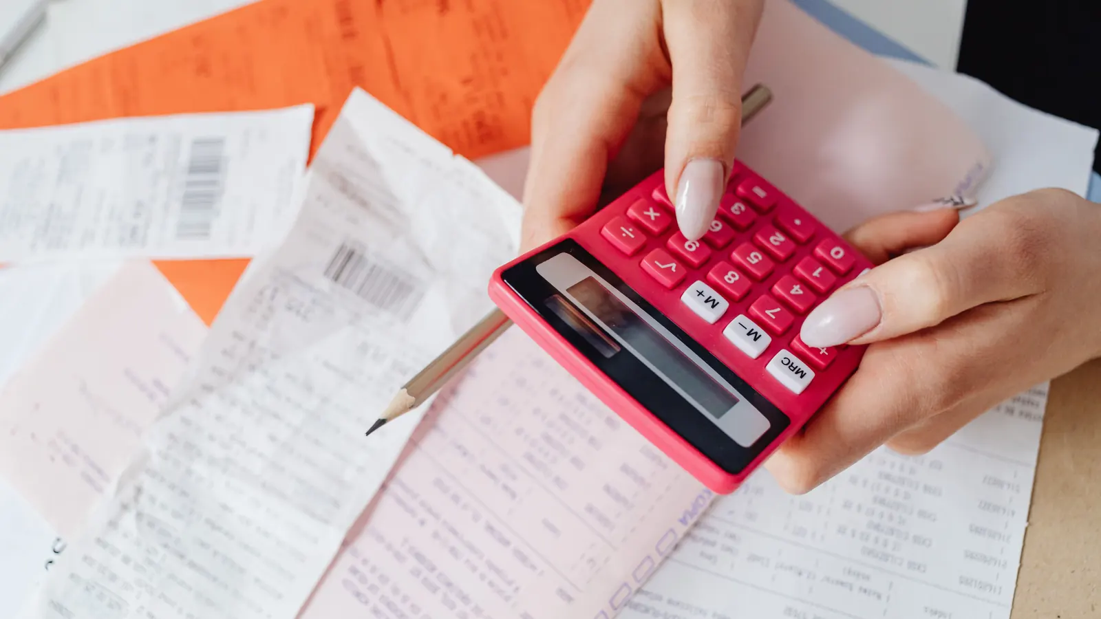 A person holding a calculator over a spread of receipts and printed forms