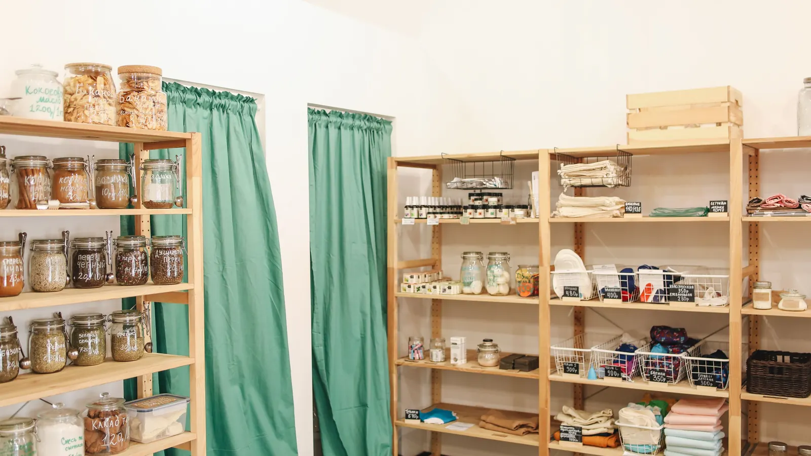 Wooden shelves stocked with jars and homewares in a bright small shop with green curtains