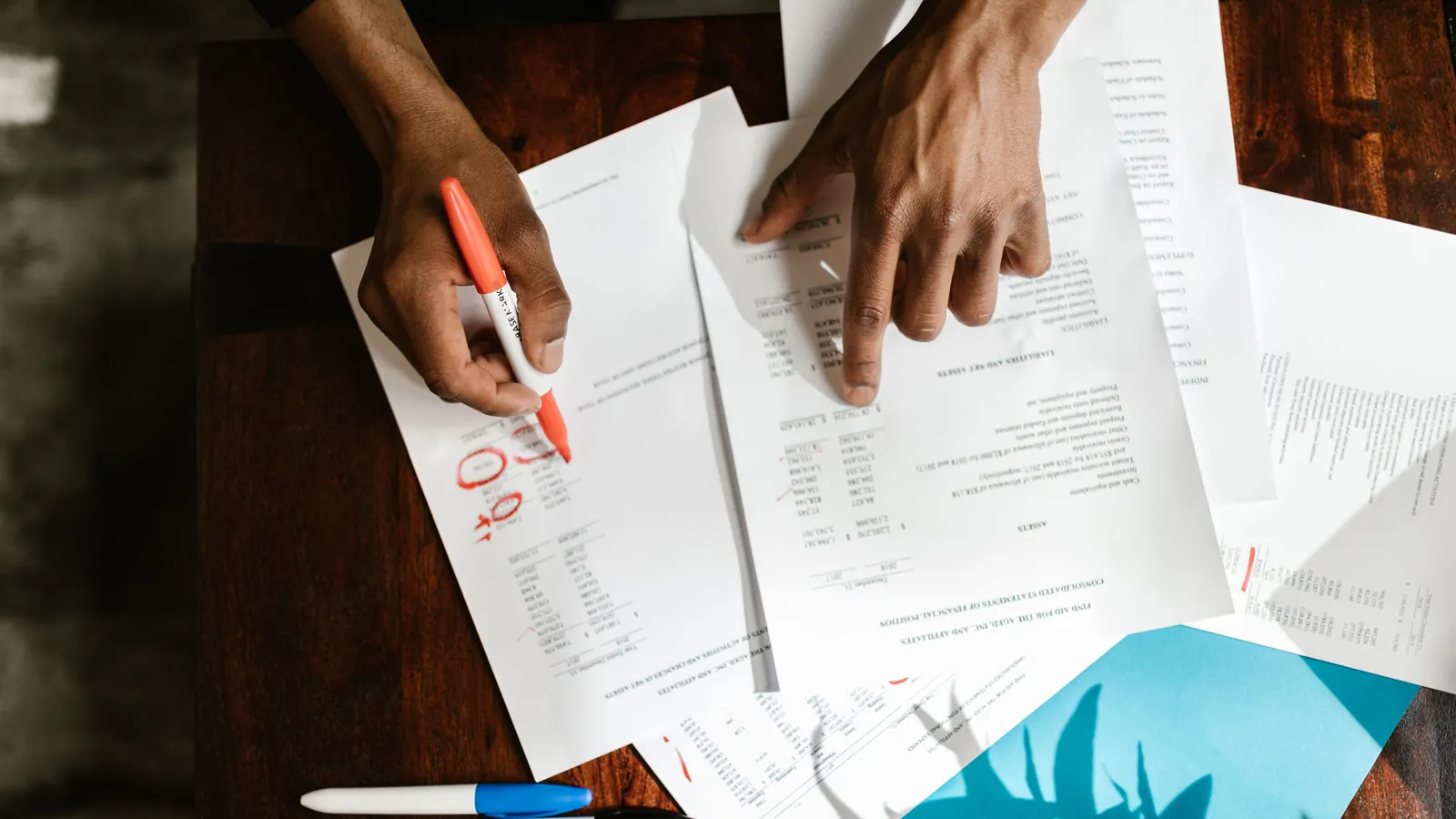 Hands reviewing financial statements and marking figures with a red pen