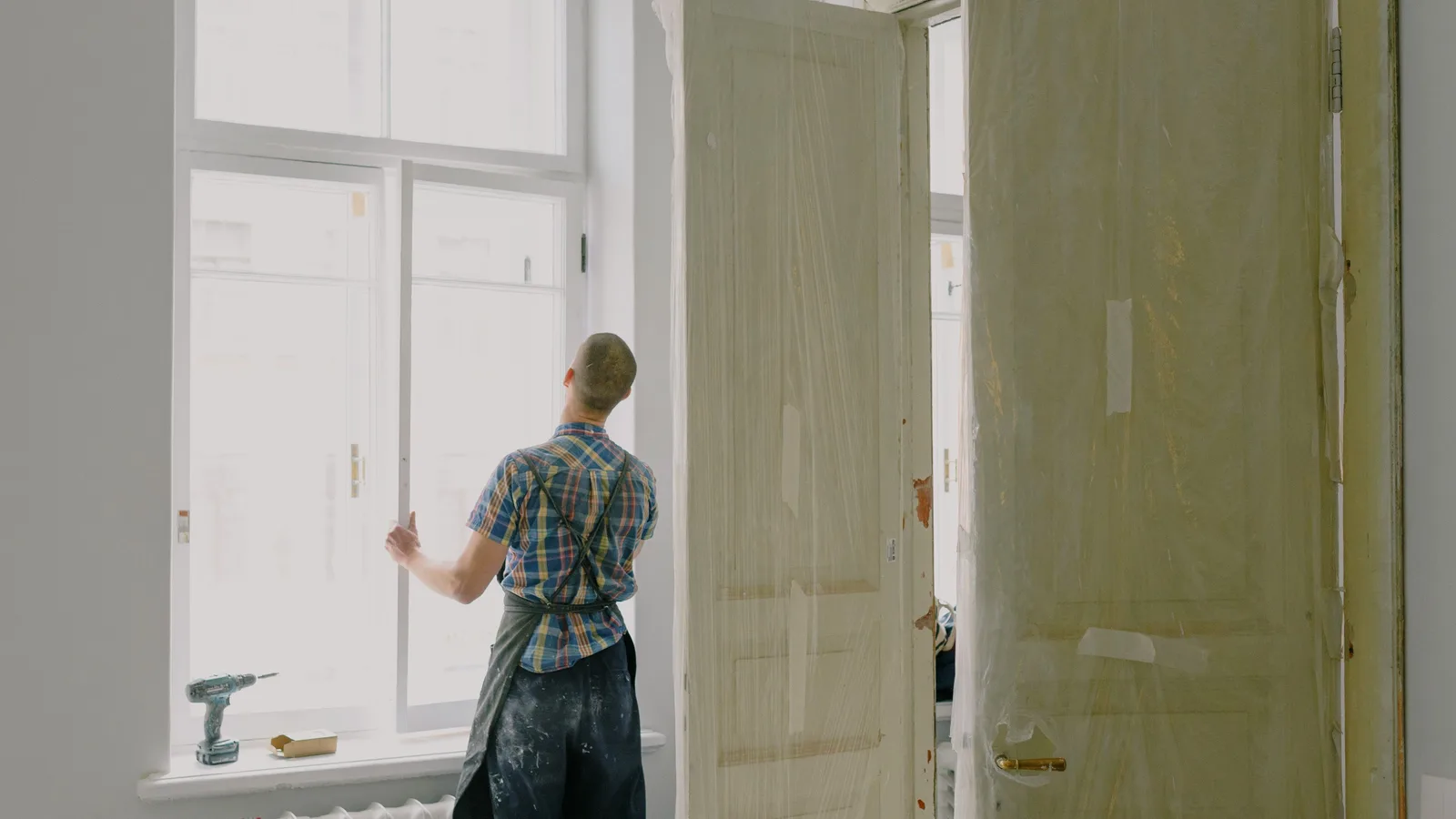 Tradesperson viewed from behind, holding a window frame during a home renovation