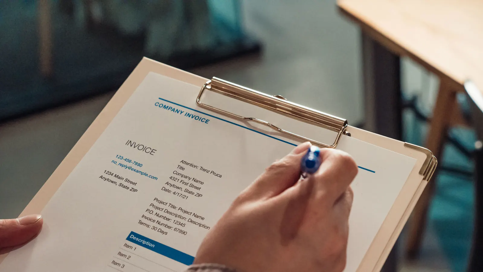 Close-up of a hand signing a company invoice showing 30-day payment terms on a clipboard