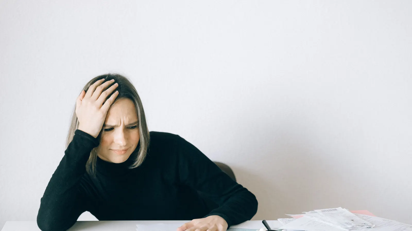 A business owner looking concerned at a desk covered in unpaid invoices